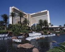 Mirage Hotel and Casino. View across waterfall and palm tree lined rock pool to hotel entrance.