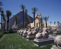 Luxor Hotel and Casino Pyramid shaped building with Sphinx and row of stone rams on lawns beside a palm lined avenue