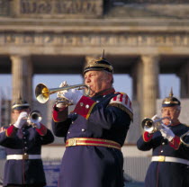 Brass bandsmen in traditional uniform playing trumpet with the Brandenburg Gate behind