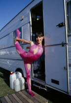 Female acrobat in pink bodysuit in arabesque position in doorway of caravan at Chipperfields Circus.