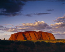 Ayers Rock.  Giant red rock formation at dusk overshadowed by storm clouds
