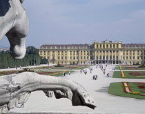 Schonbrunn Palace and tourists walking in the formal gardens with a stone equestrian statue in the foreground