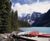 Canoes on a jetty beside the pine tree lined lake with snow caped mountains beyond
