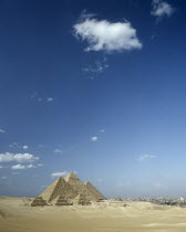Pyramids in desert landscape with shadows cast over sand and Cairo beyond.