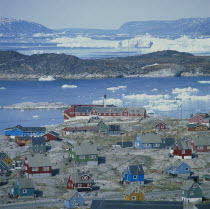 View over Ilulissat town with the sea and icebergs beyond coloured houses on rock