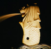 Floodlit statue spouting water at night.