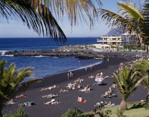 Playa de la Arena near Los Gigantes with sunbathers on black sandy beach and apartments in the distance