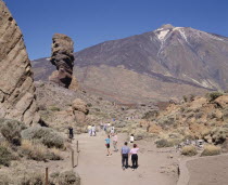 Mount Teide National Park with tourists on dry and dusty path amongst rock formations with Teide in the distance