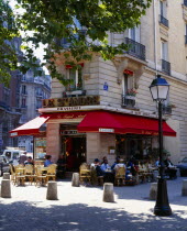 Cafe on street corner with red awning and outside tables street lamp and tree.