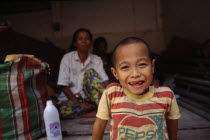 Karen refugee boy smiling in foreground with mother in the background
