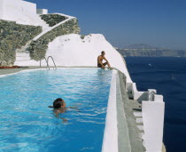 Imerovigli.  Couple in swimming pool overlooking sea. Thira