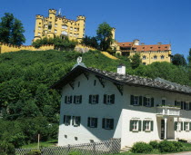 Hohenschwangau Castle on hillside overlooking white painted building with window shutters and balcony.Bavaria Bayern