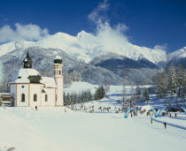 Church in winter landscape with skiing competition taking place in middle foreground and snow covered mountain backdrop.Tyrol