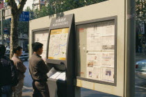 Nanjing Road.  Men reading map and newspapers displayed on boards in  news windows  on the street.