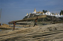 Unloading lengths of cane on the banks of the Ayeyarawady overlooked by temple behind.Burma