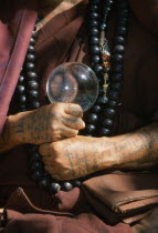 Cropped vew of Buddhist monk from The Golden Horse Forest Monastery showing tattooed arms and hands and prayer beads.Thai/Burmese border.
