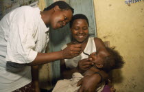 Young child held by mother receiving medicine on spoon.