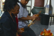 Man with son kneeling before an altar shaking containers of fortune sticks