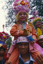 Shan Poi San Long. Crystal Children ceremony with Luk Kaeo in costume sitting on mans shoulders at Wat Pa Pao