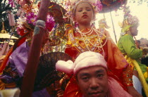 Shan Poi San Long. Crystal Children ceremony with Luk Kaeo in costume sitting on mans shoulders at Wat Pa Pao