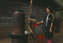 Lisu woman checking cloth filter on the spout of her still for making corn whiskey