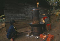 Lisu woman stoking fire of her still for making corn whiskey