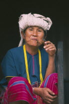 Portrait of a Karen woman sitting on the steps of her house smoking a pipe