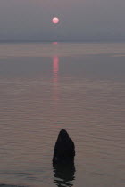 Asi Ghat. A Hindu man baths in the Ganges River with the early morning sun over the horizon