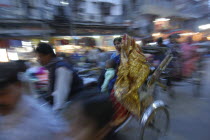 The Godaulia intersection. A passing rickshaw with two women in saris in the evening. Movement blur.