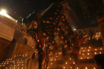 Deep Divali Festival. Men carry a paper statue of the Hindu God Ganesh down steps covered in oil lamps leading to the Ganges River