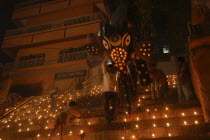 Deep Divali Festival with men carrying paper statue of Hindu God Ganesh down steps leading to the Ganges River while small boy lights oil lamps