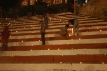 Deep Divali Festival with young boys lighting oil lamps on steps leading down to the Ganges River