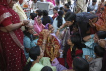 Sankat Mochan Mandir temple. Women friends and relatives cheer a bride with her head draped in a red sari at her wedding outside the temple