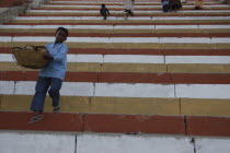 Boy carrying basket down steps to a ghat on the Ganges River