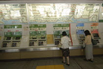 Ueno train station with women buying train tickets from vending machines with the train route map above