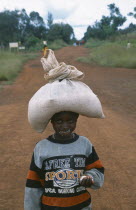 Young refugee girl carrying sack of food on her head with remnants of food all around her mouth.