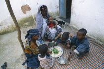 Woman and children eating lunch from communal dish using the right hand.  At a family meal men are usually served first and women and children eat seperately later.