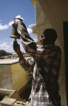 Gacmodhere primary School.  Male teacher ringing school bell.