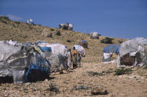 The Kandahr IDP camp for Internally Displaced Persons.  Women and child standing between huts on barren hillside.     Ayaha  returnee settlement