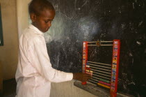 Boy using an abacus in school classroom with blackboard on wall behind.