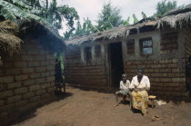 Refugee woman and child sitting outside thatched  mud brick home in camp.