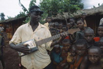 Refugee children listening to boy playing guitar made from cooking oil can.