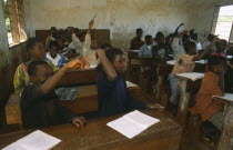 School for refugee children in Great Lakes camp.  Children at desks in classroom with raised hands.