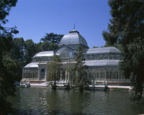 Retiro Park. The Crystal Palace surrounded by trees seen from across pond.