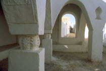 Tarasan Square.  Arched window in wall of passageway framing white painted town walls and man on bicycle.Ghadamis Gadames