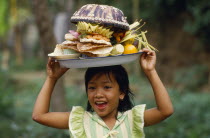 Laughing Balinese girl carrying food offerings on her head.