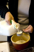 Woman age 30 measuring milk as an ingredient in a mixing bowl for waffles.