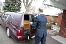 Funeral director closing back door of hearse on coffin.