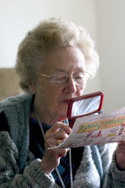 Elderly woman reading an article with a magnifying lens.Aunt Fran age 92 suffering from macular degeneration a breakdown of light-sensitive cells in the central area of the retina making reading and...
