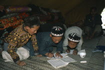 Kirghiz children writing inside yurt with man sitting beside doorway behind.Ger